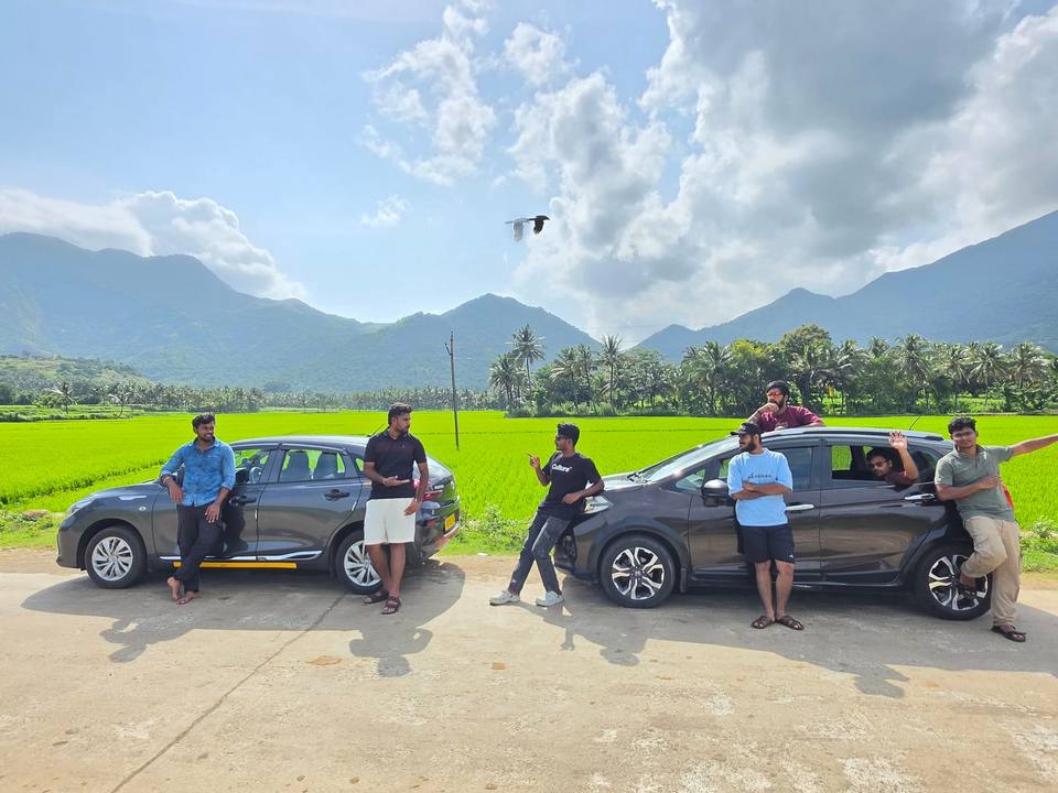 Our Glanza and WR-V parked by green paddy fields below the hills, with Naveen and friends on their Tenkasi trip